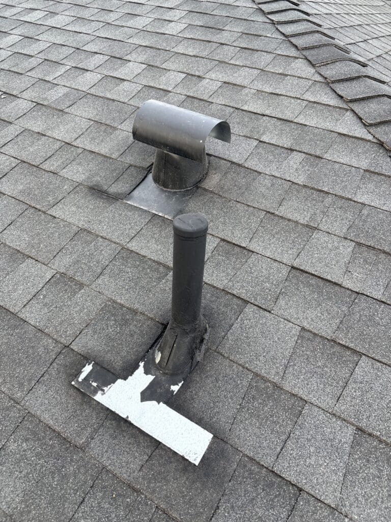 Roof plumbing vent with peeling flashing coating and messy sealant on a new asphalt-shingle roof
