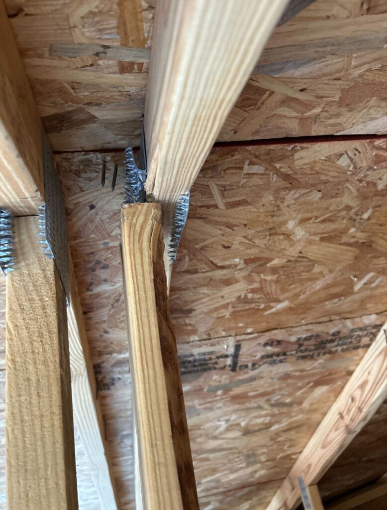 Failed metal truss connector plate pulled away from framing lumber in a new-home attic